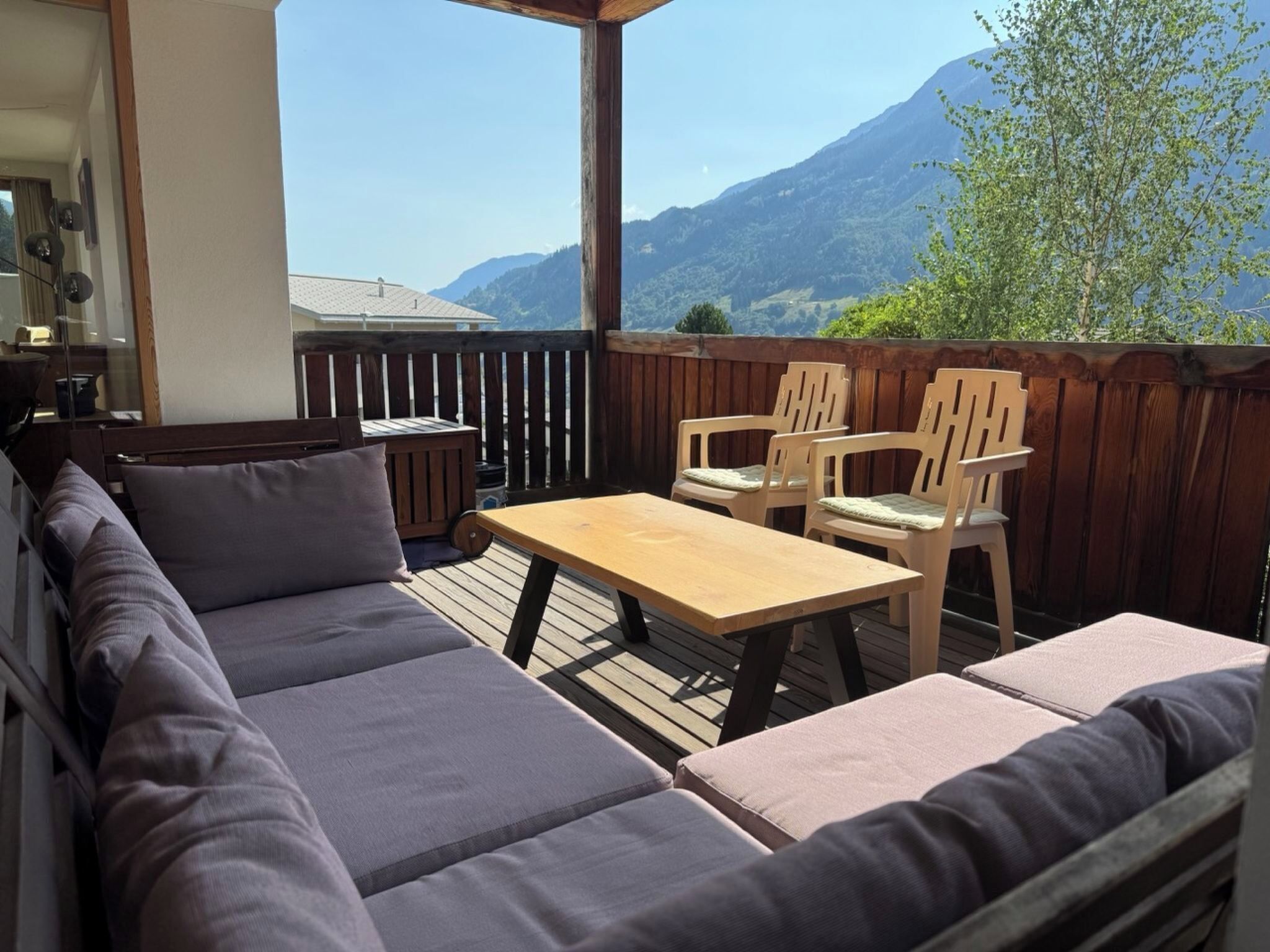 Ein Sitzbereich im Freien mit einem Holztisch und -stühlen, einer gepolsterten Couch und Blick auf Berge.