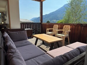 An outdoor seating area with a wooden table and chairs, a cushioned sofa, and a view of mountains.
