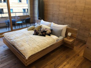 Ein modernes Schlafzimmer mit einem Holzbett, einem Nachttisch und Blick auf den Balkon.