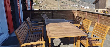 An outdoor wooden deck with a table and benches, overlooking a mountainous landscape.