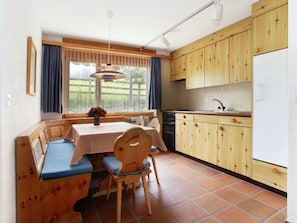 Eine kleine Küche mit Holzausstattung, ein Essbereich mit einer Bank und ein Fenster mit Vorhängen.