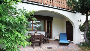 Une terrasse avec une table et des chaises, un fauteuil bleu et une porte en bois.