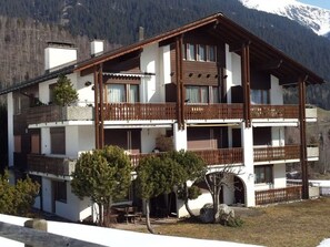A two-story chalet with balconies, surrounded by trees and mountains. - Casa Sax 5 Church, (Disentis/Mustér), 1628 by Interhome (Disentis)