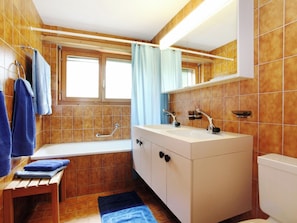 A bathroom with a bathtub, a sink, a mirror, and a window. - Casa Sax 5 Church, (Disentis/Mustér), 1628 by Interhome (Disentis)