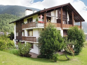 A multi-story building with balconies, surrounded by greenery and mountains in the background. - Casa Sax 5 Church, (Disentis/Mustér), 1628 by Interhome (Disentis)