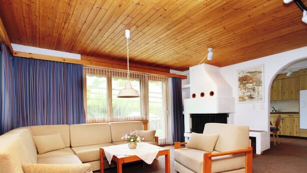 Un salon avec un plafond en bois, un canapé, un fauteuil, une table avec un vase et une cheminée.
