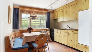 Une cuisine de taille réduite avec des meubles de rangement en bois, une table à manger avec des bancs et une fenêtre agrémentée de rideaux.