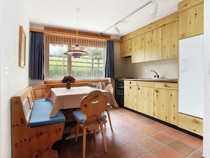 A compact kitchen with wooden cabinets, a dining table with benches, and a window with curtains. - Casa Sax 5 Church, (Disentis/Mustér), 1628 by Interhome (Disentis)