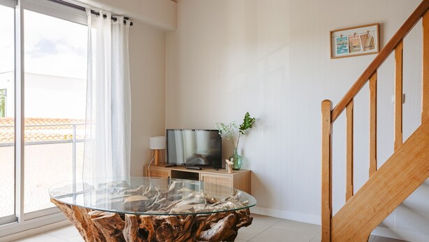 Een moderne woonkamer met een glazen salontafel, een televisie en een houten trap.