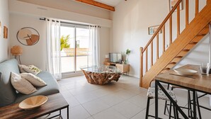 Een moderne woonkamer met een salontafel met glazen blad, een houten trap en een bank met kussens.