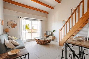 A modern living room with a glass-top coffee table, a wooden staircase, and a sofa with cushions. - La Parenthèse Rochelaise (with Parking Space) by Kaz'Concept (La Rochelle)