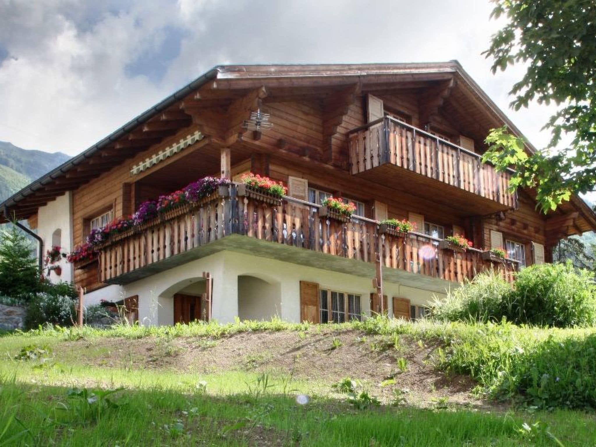 Eine Holzhütte mit Balkonen, umgeben von Grün und Bergen.