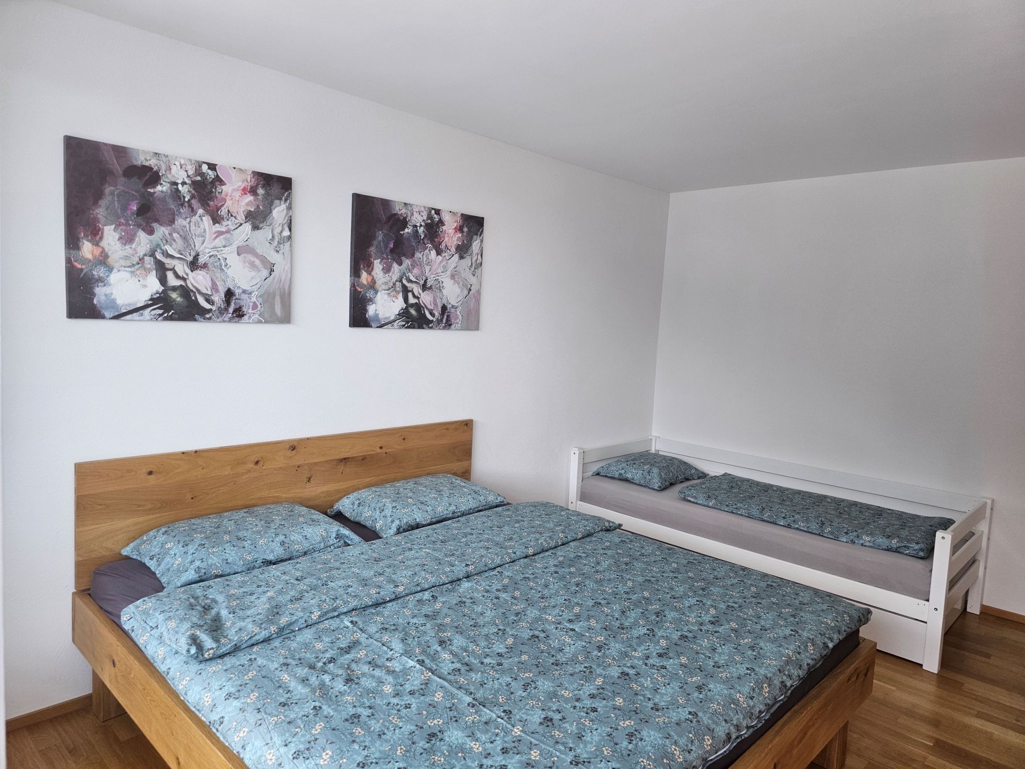 A bedroom with a wooden bed, a smaller bed, and two abstract paintings on the wall.