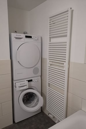 A compact laundry room with a front-loading washing machine and dryer, a built-in heater, and a small storage cabinet. - Ladina, (Disentis/Mustér), 1724 by Interhome (Disentis)