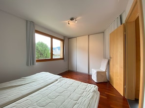 Ein Schlafzimmer mit zwei Betten, einem großen Fenster, einem Kleiderschrank und einem Sessel.
