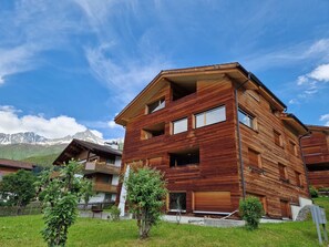 A multi-story wooden building with balconies, surrounded by greenery and mountains in the background. - Dentervitgs, (Sedrun), by Interhome (Sedrun)