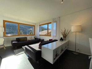 A modern living room with a sofa, a coffee table, and a cabinet. Large windows offer a view of mountains. - Dentervitgs, (Sedrun), by Interhome (Sedrun)