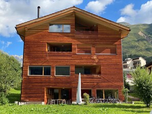 A multi-story wooden building with balconies, large windows, and a grassy foreground. - Dentervitgs, (Sedrun), by Interhome (Sedrun)