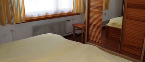 A bedroom with a bed, a chair, a wardrobe, and a window with curtains.