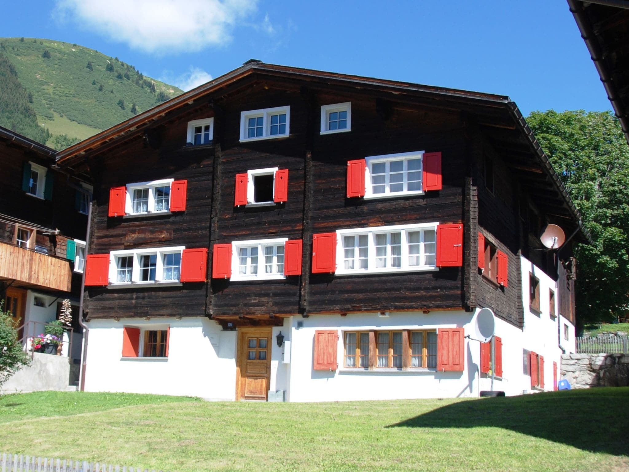 Ein mehrstöckiges Gebäude mit roten und weißen Fensterläden, einer Holzfassade und einem weißen Unterteil.