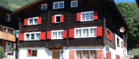 Un immeuble à plusieurs étages, avec des volets rouges et blancs, une façade en bois et une partie inférieure blanche.
