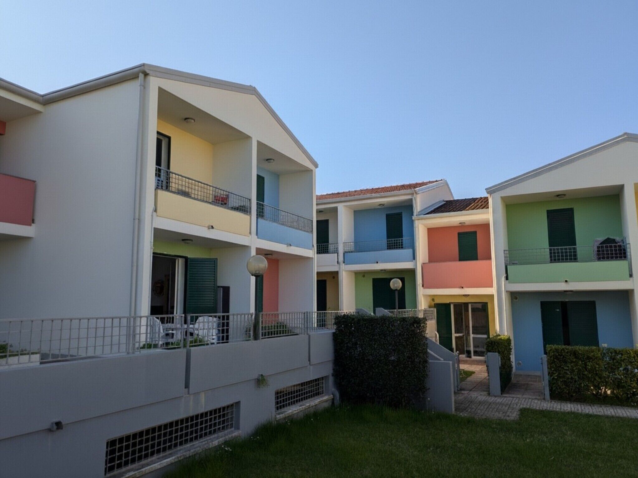 A multi-story residential building with balconies, a gated entrance, and a small garden area.