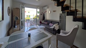A modern living room with a sofa, dining table, and chairs, a kitchen area with a refrigerator, and a staircase. - Charming Two-level Villa With Pool (Caorle)