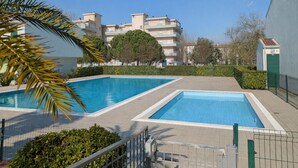 A swimming pool area with two pools, surrounded by a fence, and a building with a WC sign in the background. - Charming Two-level Villa With Pool (Caorle)