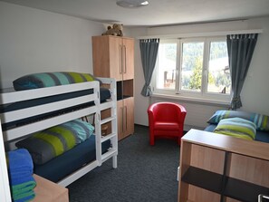 A room with bunk beds, a red chair, a wooden cabinet, and a window with curtains. - Tgèsa Pazzola Huonder-Monn, (Bugnei/Sedrun), 005.01 by Interhome (Sedrun)