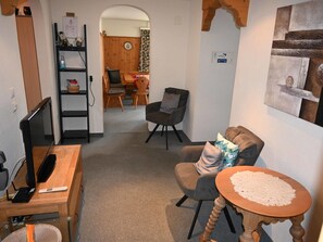 A room with a desk, a chair, a small table with a placemat, a bookshelf, and a dining area in the background. - Tgèsa Pazzola Huonder-Monn, (Bugnei/Sedrun), 005.01 by Interhome (Sedrun)