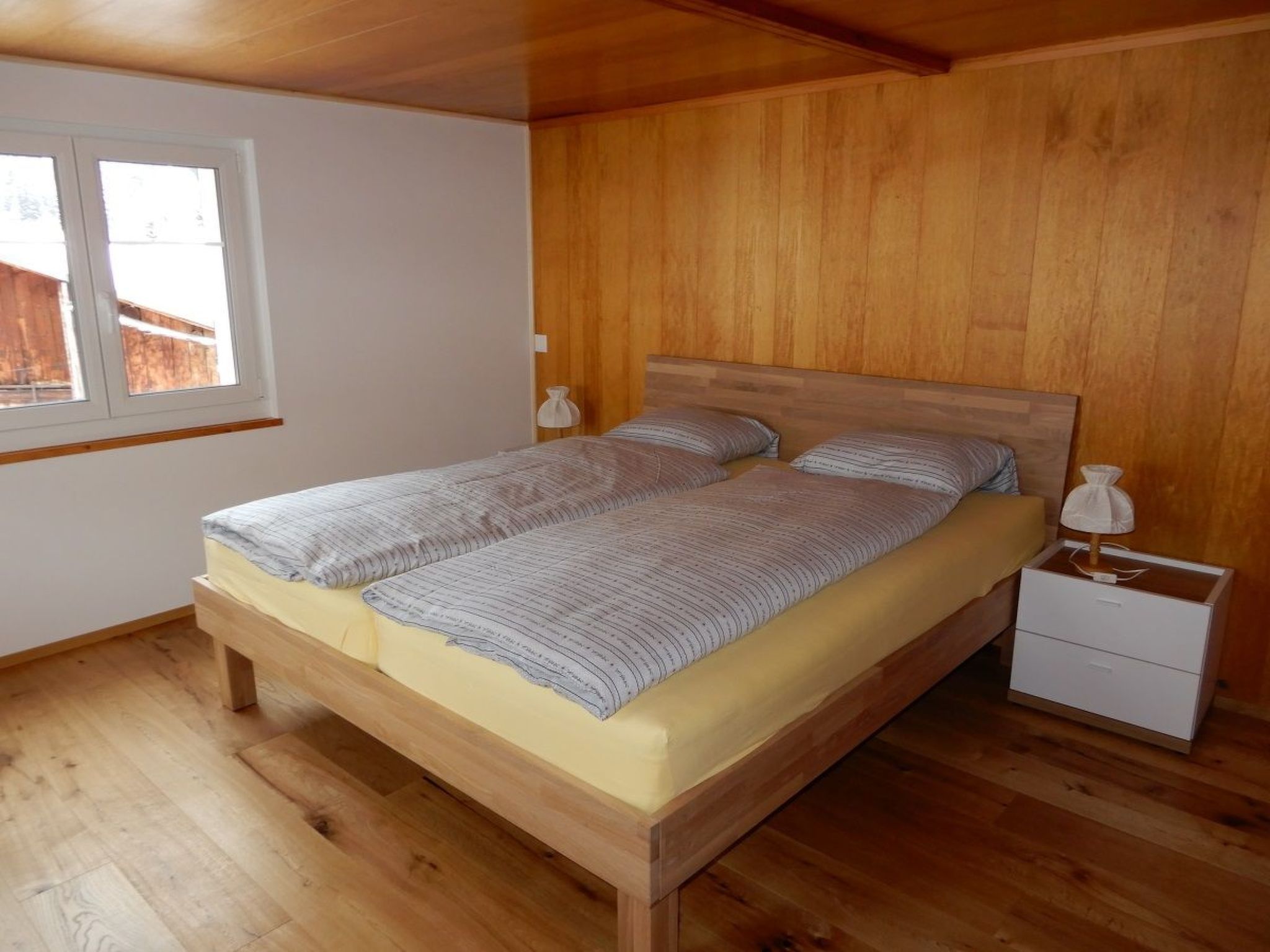 Quarto com cama de madeira, duas mesas de cabeceira e uma janela.
