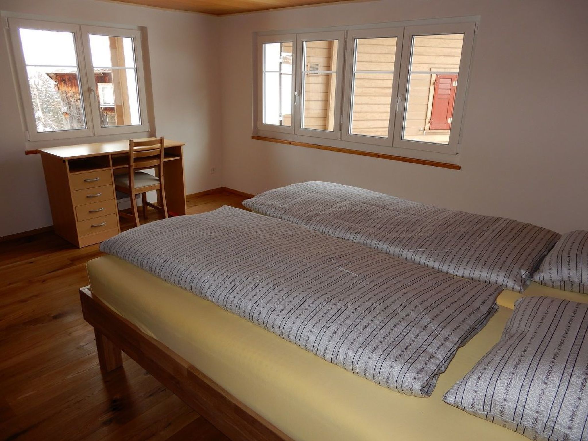 A bedroom with a wooden desk, two beds, and large windows.