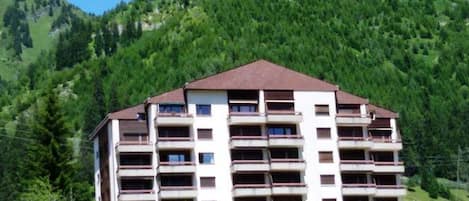 A multi-story hotel with balconies, surrounded by lush greenery and mountains.