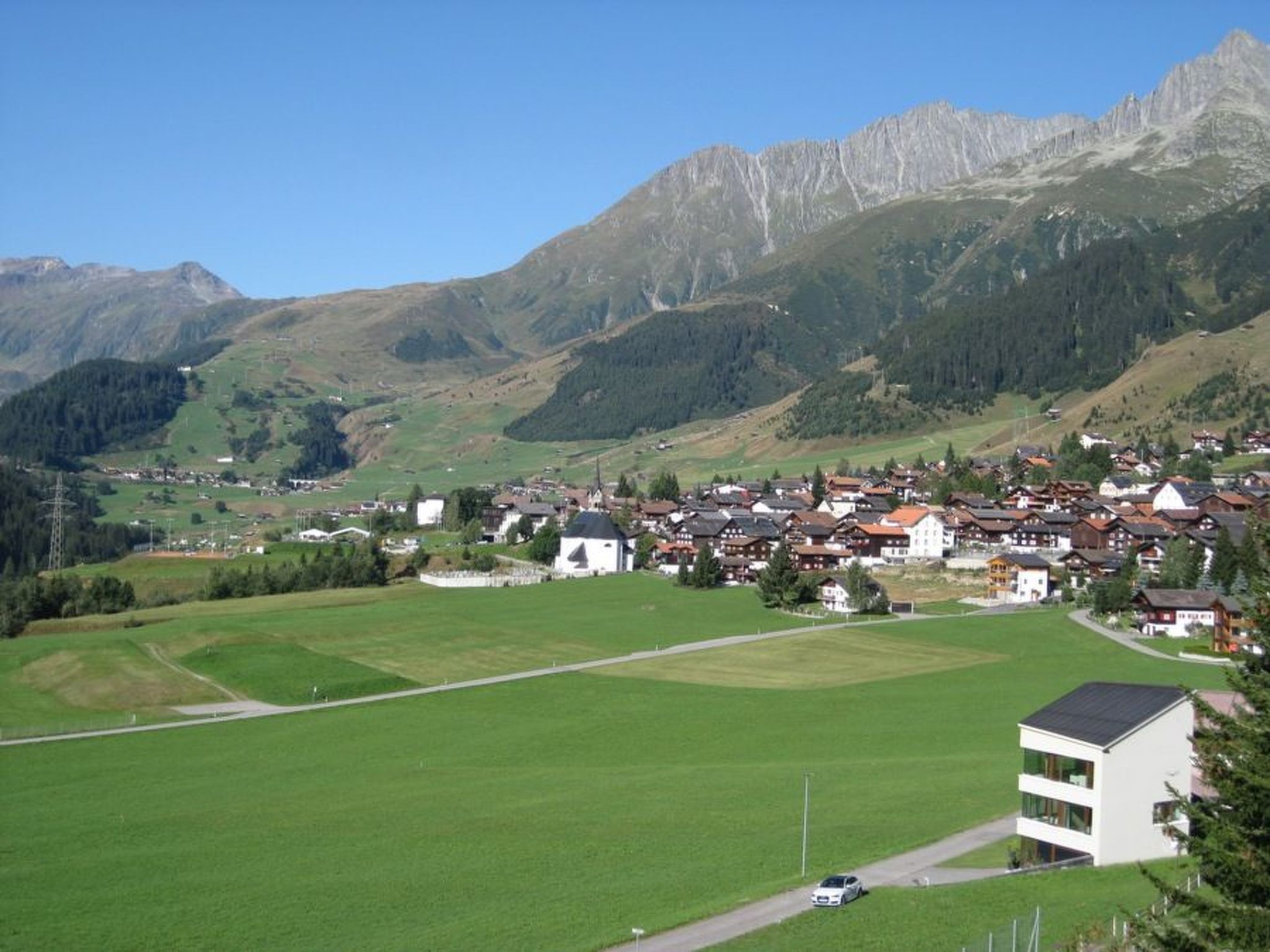 Un village avec des maisons traditionnelles, un grand champ ouvert et des montagnes en arrière-plan.