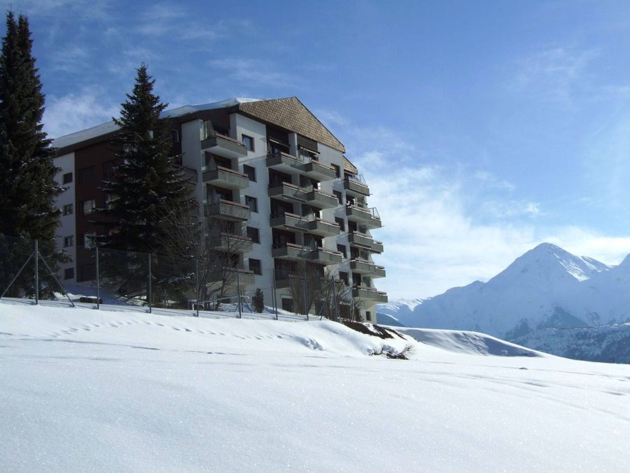 Ein mehrstöckiges Hotel mit Balkonen vor einer verschneiten Berglandschaft.