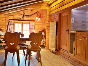 Ein Holzinnenraum mit Esstisch und Stühlen, einer Küchenzeile mit Schränken und einem Fenster mit Vorhängen.