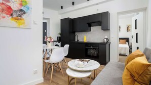 Une cuisine moderne avec des meubles noirs, un coin repas blanc doté d’une table ronde, et un canapé gris agrémenté de coussins couleur moutarde.