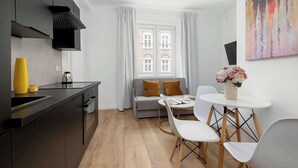 Une cuisine moderne avec des meubles noirs, un vase jaune, une machine à café et un canapé gris dans l’espace salon.