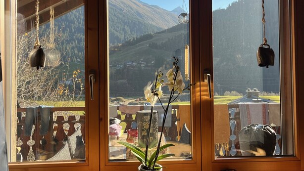 Ein Zimmer mit Holztür, Bergblick und hängenden Gegenständen.