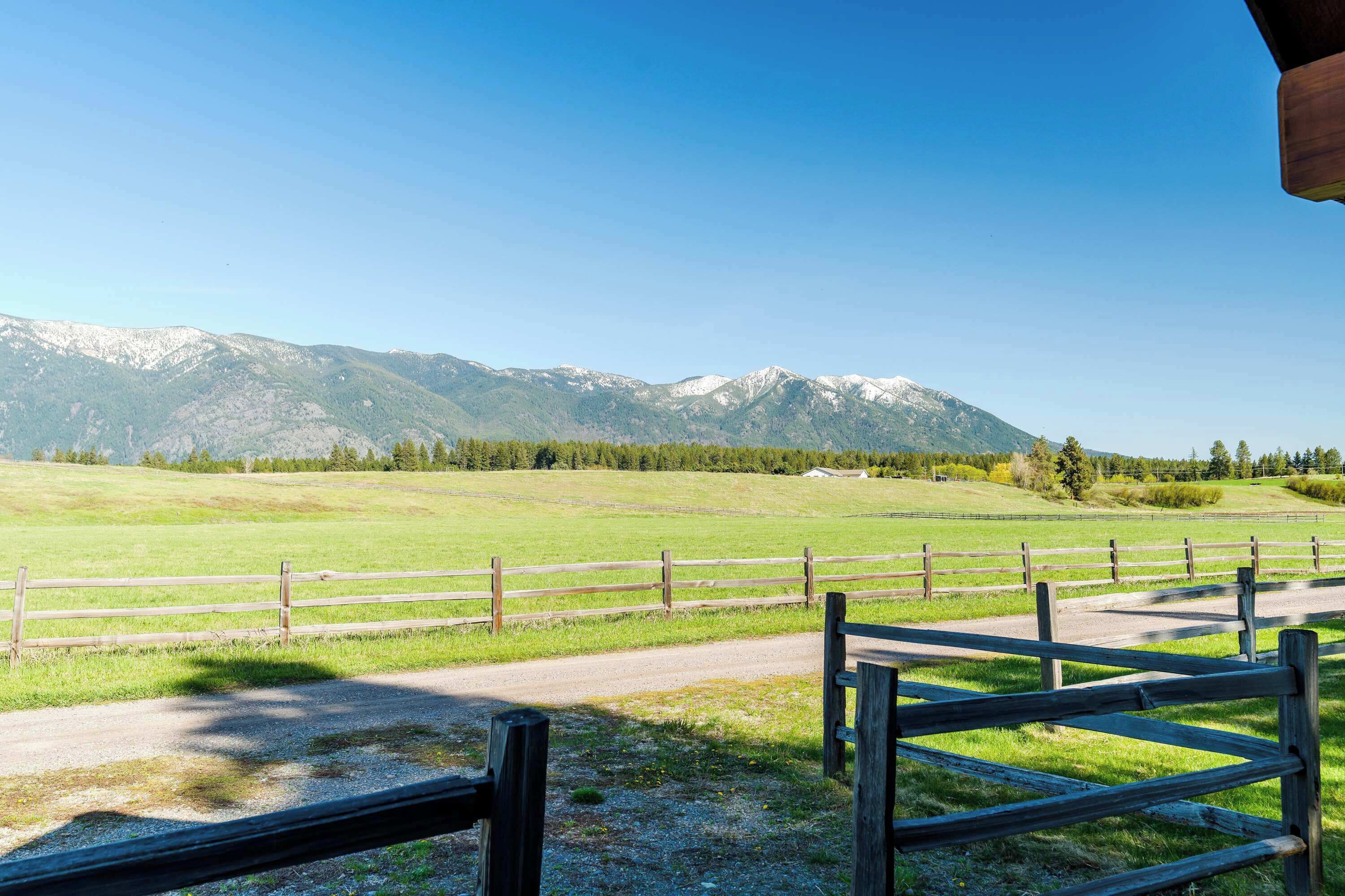 A rural landscape with a dirt road, wooden fences, and a mountain range in the background.