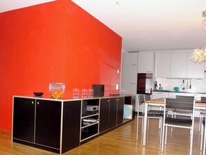 A modern kitchen with white cabinets, a dining area with a table and chairs, and a red accent wall. - Tgésa Bienviver, (Sedrun), 136.02 by Interhome (Sedrun)