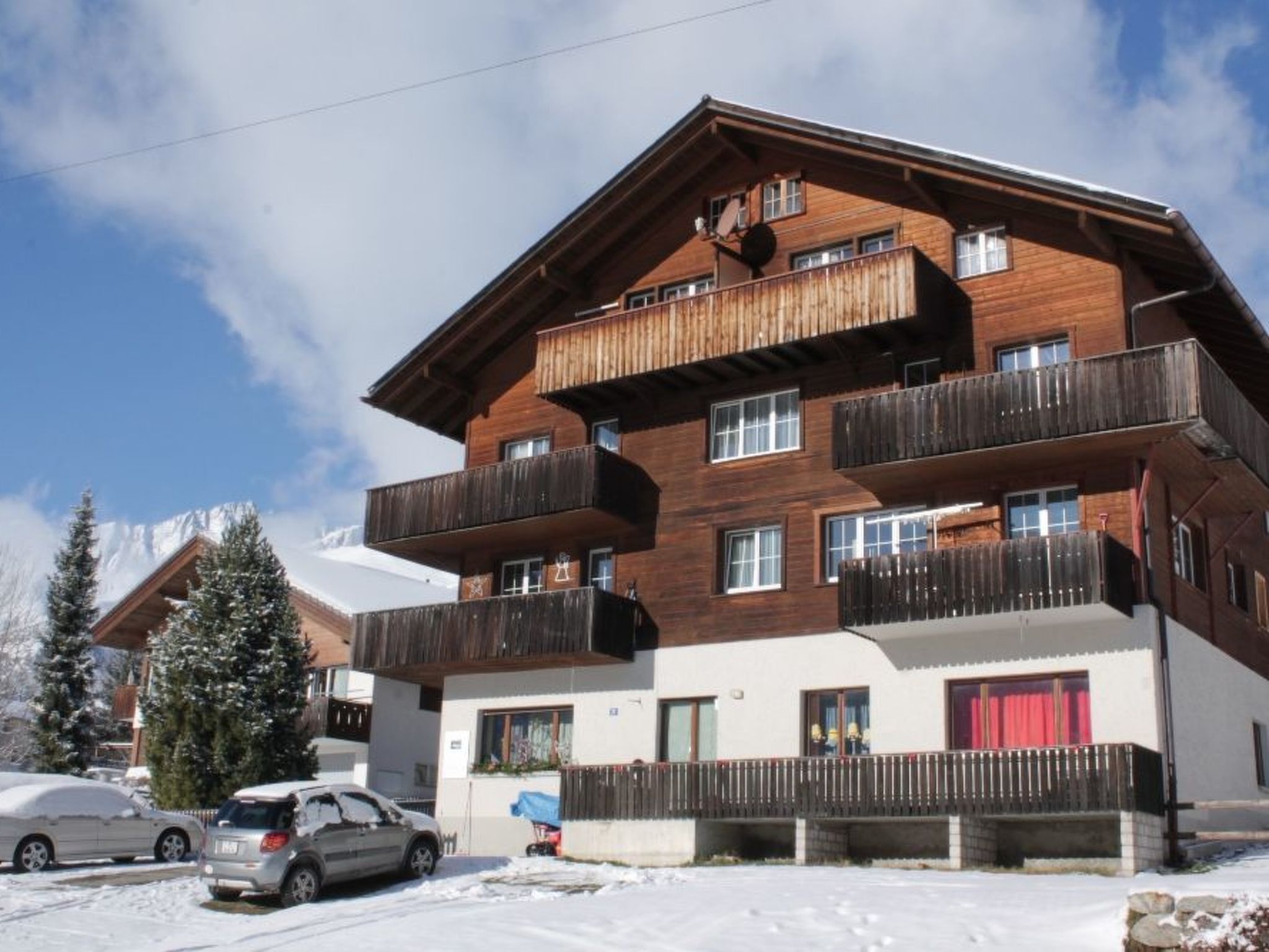 Un immeuble en bois à plusieurs étages, doté de balcons, d’un espace de stationnement et d’un sol recouvert de neige.
