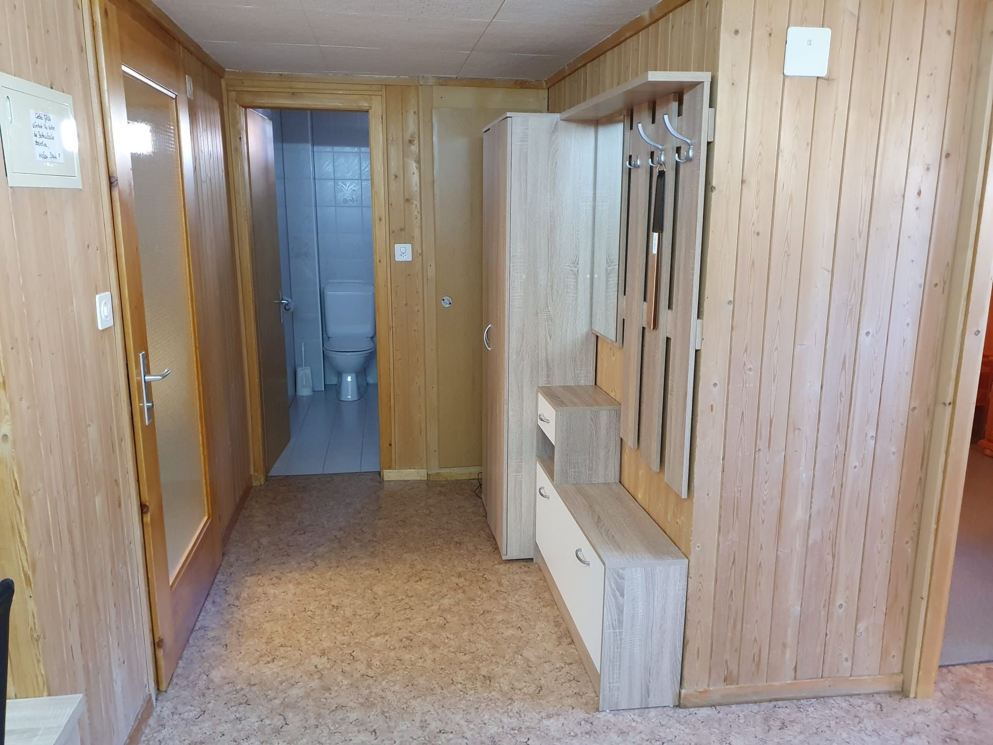 A hallway with wooden walls, a door leading to a bathroom, and a coat rack with hooks.
