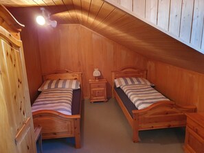 A small, wooden room with two single beds, a nightstand with a lamp, and a sloped ceiling. - Citrini, (Sedrun), 167.03 by Interhome (Sedrun)
