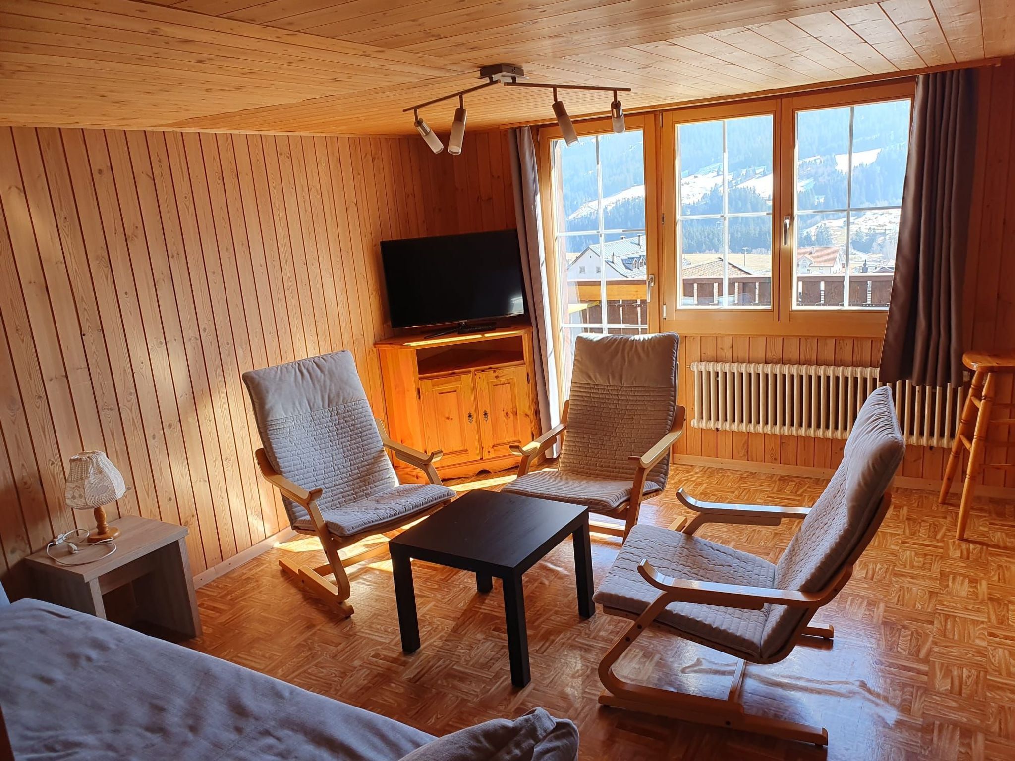 Ein gemütliches Zimmer mit Holzwänden und Holzdielen, einem Flachbildfernseher, einem Tisch und zwei Stühlen.