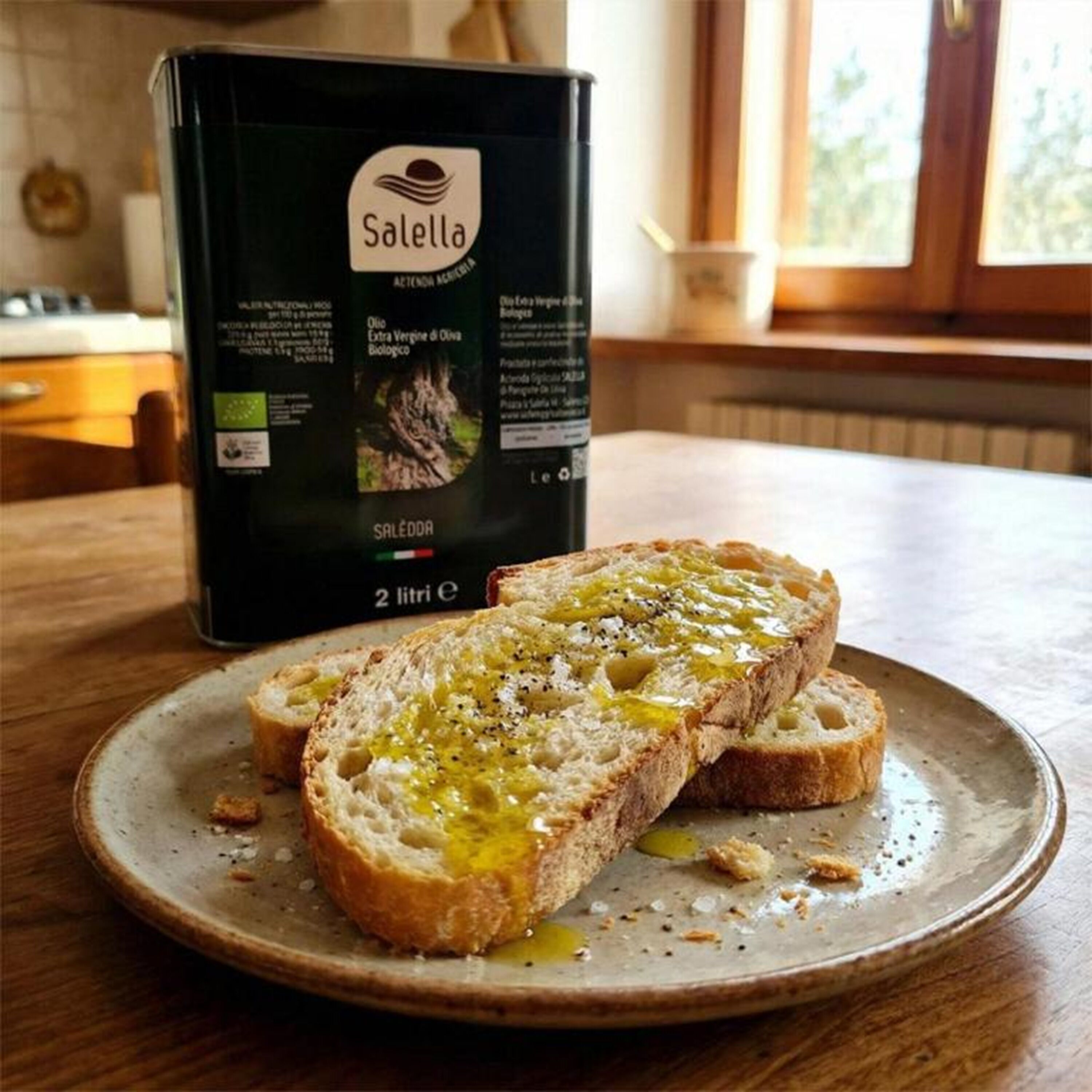 A plate with toasted bread and olive oil, a box of Salella extra virgin olive oil, and a kitchen setting.