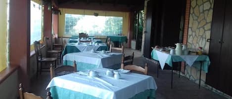 A restaurant with tables set for dining, a stone wall, and a covered outdoor area.