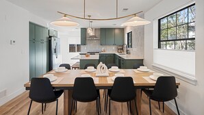 Une cuisine moderne avec un coin repas, comprenant une grande table en bois, des chaises noires et des luminaires suspendus.