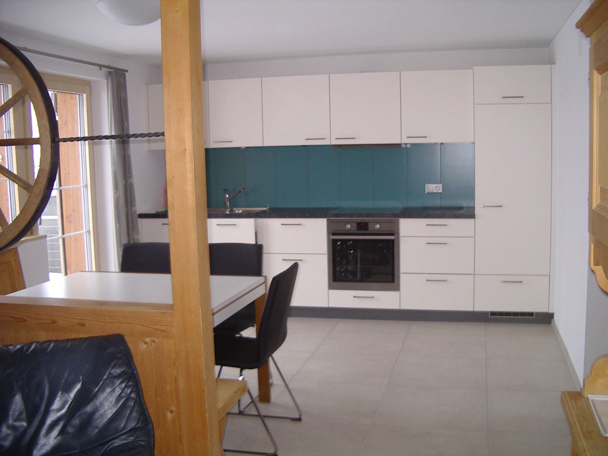 A modern kitchen with white cabinets, a black oven, and a teal backsplash.