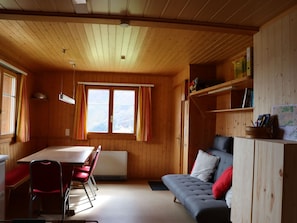 A cozy cabin interior with a dining area, a sofa, and a window with curtains. - Tgèsa Alpina Müller, (Rueras/Sedrun), 956.01 by Interhome (Rueras Dieni)